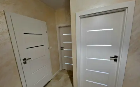 Nowoczesne drzwi Drea Auri w białym kolorze, z eleganckimi, poziomymi przeszkleniami, tworzą stylowe przejście w korytarzu.