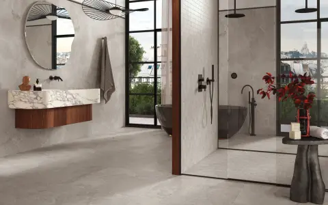 Salle de bain moderne avec baignoire îlot et douche vitrée. Le sol et les murs sont recouverts de carrelage gris, tandis que la paroi de douche est en petite faïence.