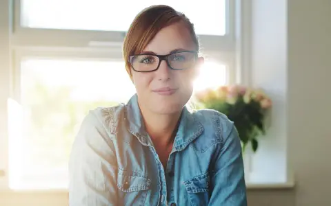 Uśmiechnięta nauczycielka w okularach, przygotowująca projekt oceny dorobku zawodowego na nauczyciela mianowanego.
