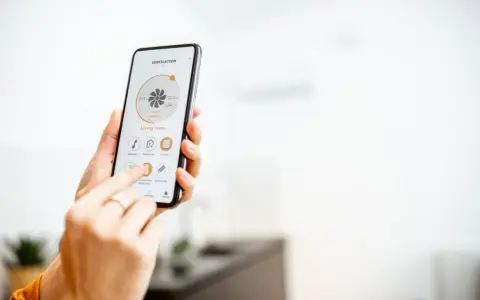 Mano usando un smartphone para encender calefacción a distancia en la sala de estar.