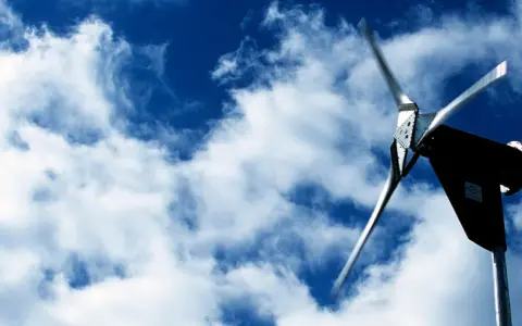 Eine Kleinwindkraftanlage in NRW dreht sich im blauen Himmel mit Wolken.