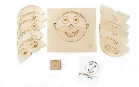 Drewniane klocki i karty do nauki emocji dla przedszkola. Zestaw zawiera elementy do tworzenia twarzy, kostkę z buźką i karty z napisem "RADOŚĆ".