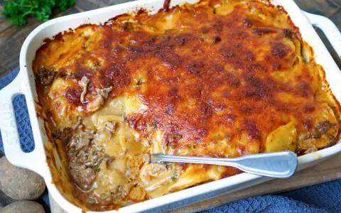 Omas Kartoffelauflauf mit Hackfleisch, goldbraun überbacken, dampft in einer weißen Auflaufform. Eine Gabel steckt in der saftigen Schicht.
