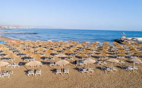 Plaża sol marina beach crete z rzędami leżaków i parasoli, gotowa na gości. Błękitne morze i niebo tworzą idealne tło.
