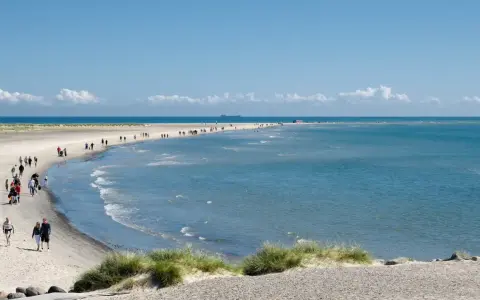En vacker strandpromenad vid Skagen, med folk som njuter av solen och havet. En perfekt resa till Skagen.