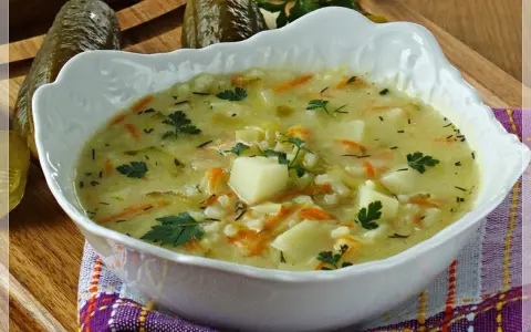 Aksamitna zupa ogórkowa na żeberkach, pełna ziemniaków, marchewki i koperku, z ogórkami w tle.