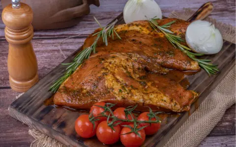 Carne marinada, lista para cocinar. El secreto ibérico se revela con romero, tomates y cebolla.
