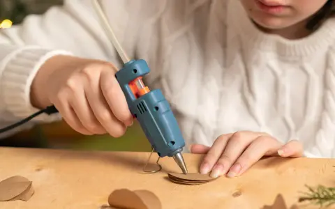 A child uses a hot glue gun to craft heart shapes from brown paper, wondering if hot glue holds up in water for their project.