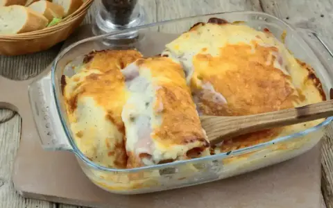 Un plat gratiné de roulés d'endives au jambon, nappés d'une sauce crémeuse et dorée, prêt à être dégusté.