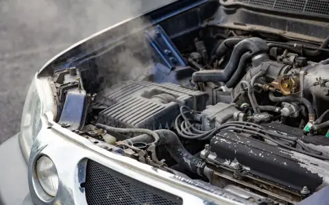 Steam rises from an overheated car radiator, indicating a potential engine problem.