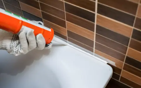 Application d'un joint acrylique ou silicone blanc pour étanchéifier le bord d'une baignoire contre un mur carrelé.