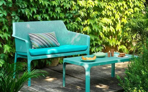 Divano e tavolino Nardi Spa Chiampo in un giardino rigoglioso, con cuscini color acqua e un set da tè.