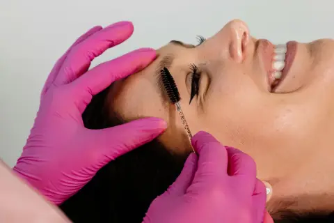 Manos con guantes rosas peinan cejas. Es parte de que es el laminado de cejas, un tratamiento para dar forma y fijar el vello.