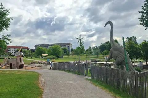 Ein riesiger Dinosaurier wacht über den Himmelsgarten mit Spielplatz.