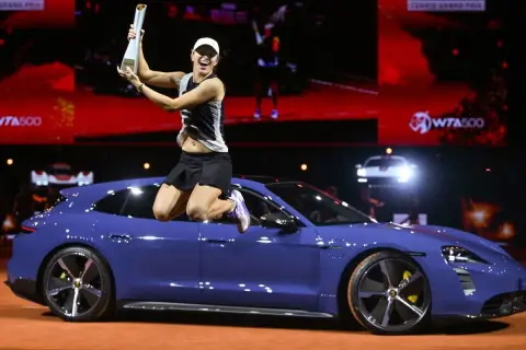 Iga Świątek skacze z pucharem na dachu niebieskiego Porsche, świętując zwycięstwo.