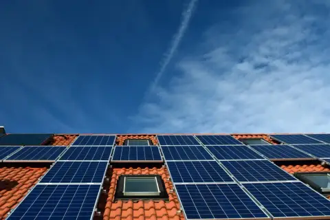 Nowoczesna instalacja PV na dachu z dachówką, pod błękitnym niebem. Panele słoneczne zbierają energię.