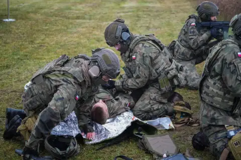 Żołnierze udzielają pomocy rannemu koledze na trawie. Kategoria e: szkolenie medyczne w terenie.