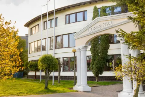 Elegancki budynek Doris Spa w Kołobrzegu z kolumnowym wejściem i kwitnącymi drzewami.