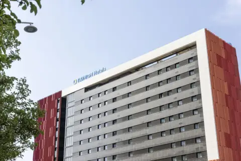 Edificio moderno con el logo "ILUNION Hotels" en la parte superior. Fachada gris con ventanas y detalles rojos.