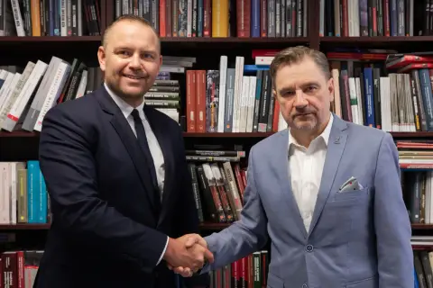 Dwóch mężczyzn w garniturach ściska sobie dłonie na tle regałów z książkami. Czy wybór Karola Nawrockiego na kandydata był konsultowany z Andrzejem Dudą?