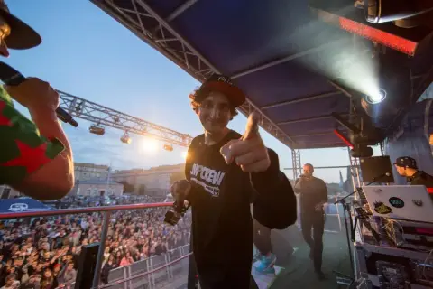 Kosi z JWP Crew w wieku około 30 lat, na scenie z mikrofonem, wskazuje palcem na widownię.