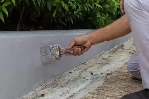Malowanie betonowego murku na zewnątrz. Szara farba do betonu na zewnątrz zapewnia trwałą ochronę.