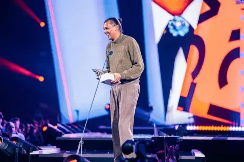 Stromae z nagrodą na scenie, jakby śpiewał "Papaoutai tekst po polsku".