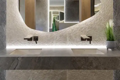Nowoczesna łazienka z dwoma umywalkami, kamiennymi płytkami i rośliną, idealnie oddająca zasady biophilic design.