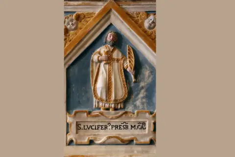 Rzeźba św. Lucifera, prezbitera, w białej szacie z palmą męczeństwa i kielichem. Nad nim dwa aniołki.