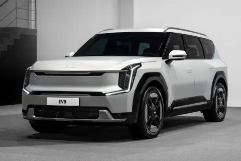 Biały, futurystyczny SUV Kia EV9 z charakterystycznymi światłami LED i masywnymi felgami stoi na szarym tle.