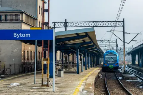 Niebieski pociąg na stacji Bytom, zadaszony peron i budynek dworca.