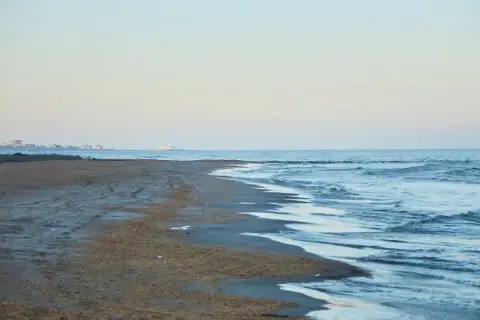 Plaża nad morzem Kaspijskim, które wysycha. W oddali widać zabudowania.
