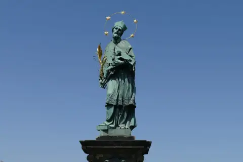 Pomnik św. Jana Nepomucena z gwiazdami nad głową i palmą męczeństwa w dłoni, na tle błękitnego nieba.