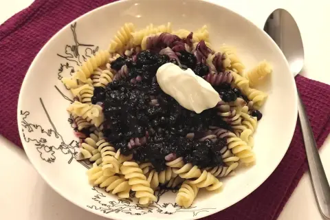 Fusilli z jagodami i kleksem śmietany na talerzu z czarnymi wzorami.