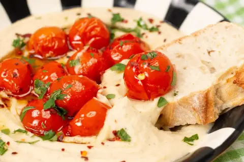 Cremiger veganer Tomatenaufstrich mit gerösteten Kirschtomaten, Kräutern und Brot.