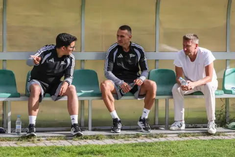 Trzech mężczyzn siedzi na ławce. Dwóch w strojach sportowych, jeden w białej koszulce. To trener Lechii Gdańsk i jego współpracownicy.