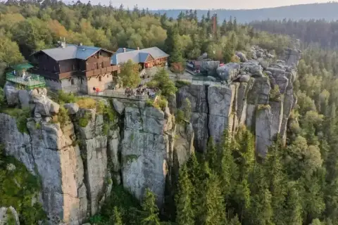 Schronisko na skalnej półce, otoczone lasem, z widokiem na wysokie góry.