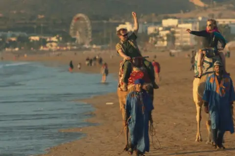 Wycieczka na wielbłądach po plaży, jak z filmu all inclusive. W tle wesołe miasteczko i tłum ludzi.