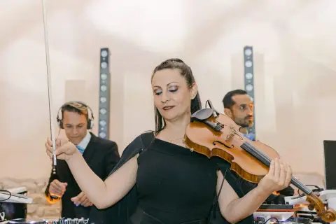 Une violoniste joue lors d'un mariage, avec des DJs en arrière-plan. Un prix DJ mariage pour une ambiance unique.