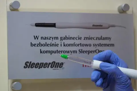Ręka w niebieskiej rękawiczce trzyma aplikator z bupiwakainą, obok tablica informująca o bezbolesnym znieczuleniu komputerowym SleeperOne.