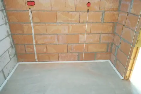 Przewody w posadzce bez peszla, przygotowane do dalszych prac instalacyjnych. Widoczne puszki elektryczne w ścianie z cegły.