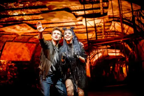 Para z musicalu "We Will Rock You" w polskim tłumaczeniu, pozdrawia publiczność na tle scenografii.