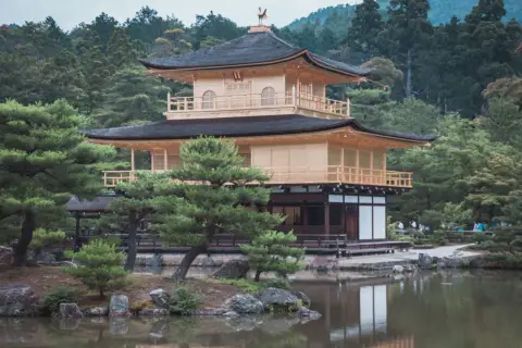 Złoty Pawilon Kinkaku-ji w Kioto, otoczony zielenią i odbijający się w stawie.