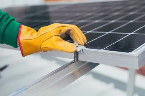 Ręka w żółtej rękawicy dokręca śrubę mocującą panel słoneczny. To ważny krok, by wiedzieć, jak dobrać falownik do instalacji.