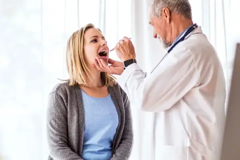 Lekarz bada gardło pacjentki. To ważny krok w diagnozowaniu, czy potrzebny jest urlop zdrowotny dla kogoś, kto źle się czuje.