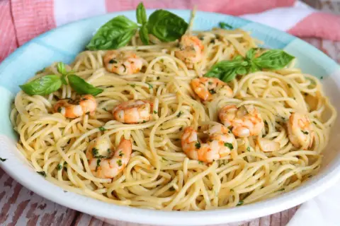 Un plato de espaguetis con gambas, adornado con hojas de albahaca fresca y perejil picado.