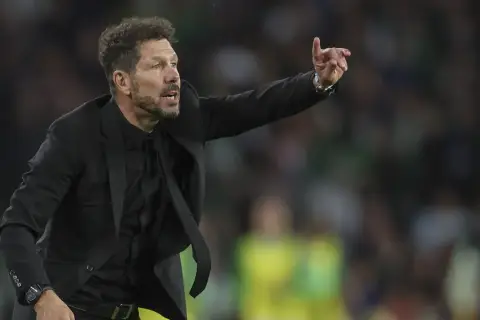 Cholo, trener Atletico Madryt, w czarnym garniturze gestykuluje na boisku, wskazując coś swoim zawodnikom.
