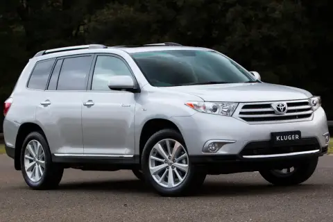Srebrny Toyota Kluger zaparkowany na drodze, z ciemnym tłem drzew.