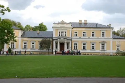 Pałac w Ciechanowcu, jedna z atrakcji regionu, otoczony zielenią. Grupa osób zwiedza teren.