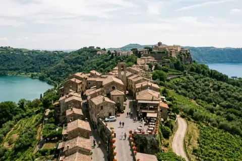 Borgo medievale sui Colli Albani, con case in pietra, un lago azzurro e uliveti rigogliosi.